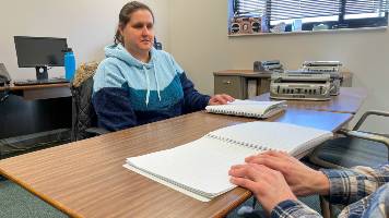 two people sitting at  a wodden table, reading braille. 